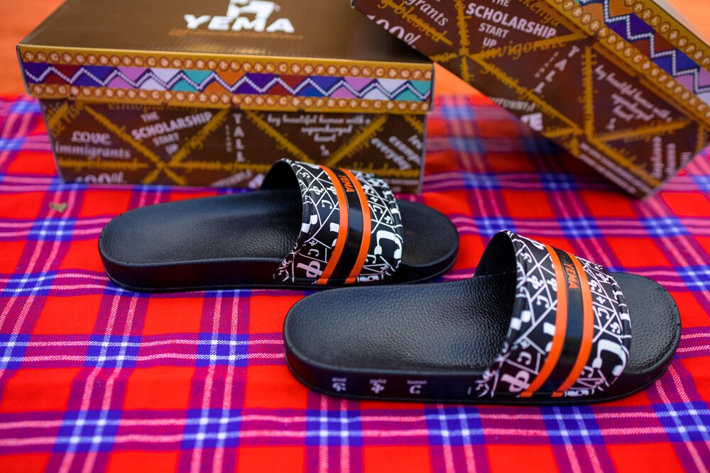 YEMA FIKIR slides in Addis Black featuring Amharic love pattern and signature orange black stripes