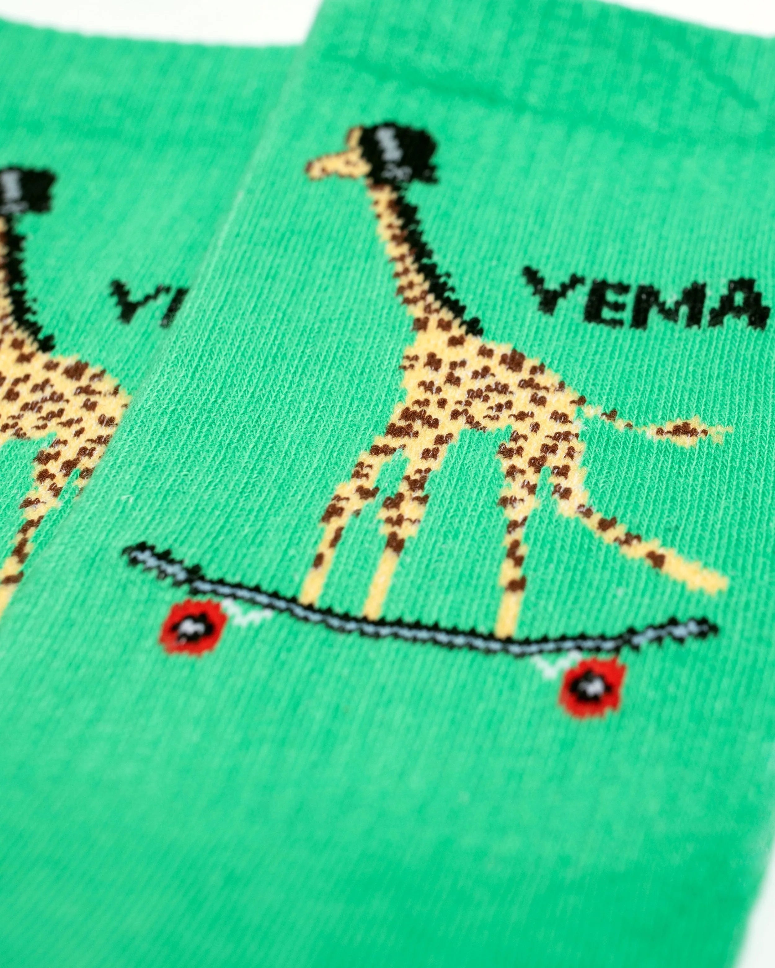 Close-up of YEMA giraffe skating socks in Kibera Green with iconic giraffe on skateboard graphic