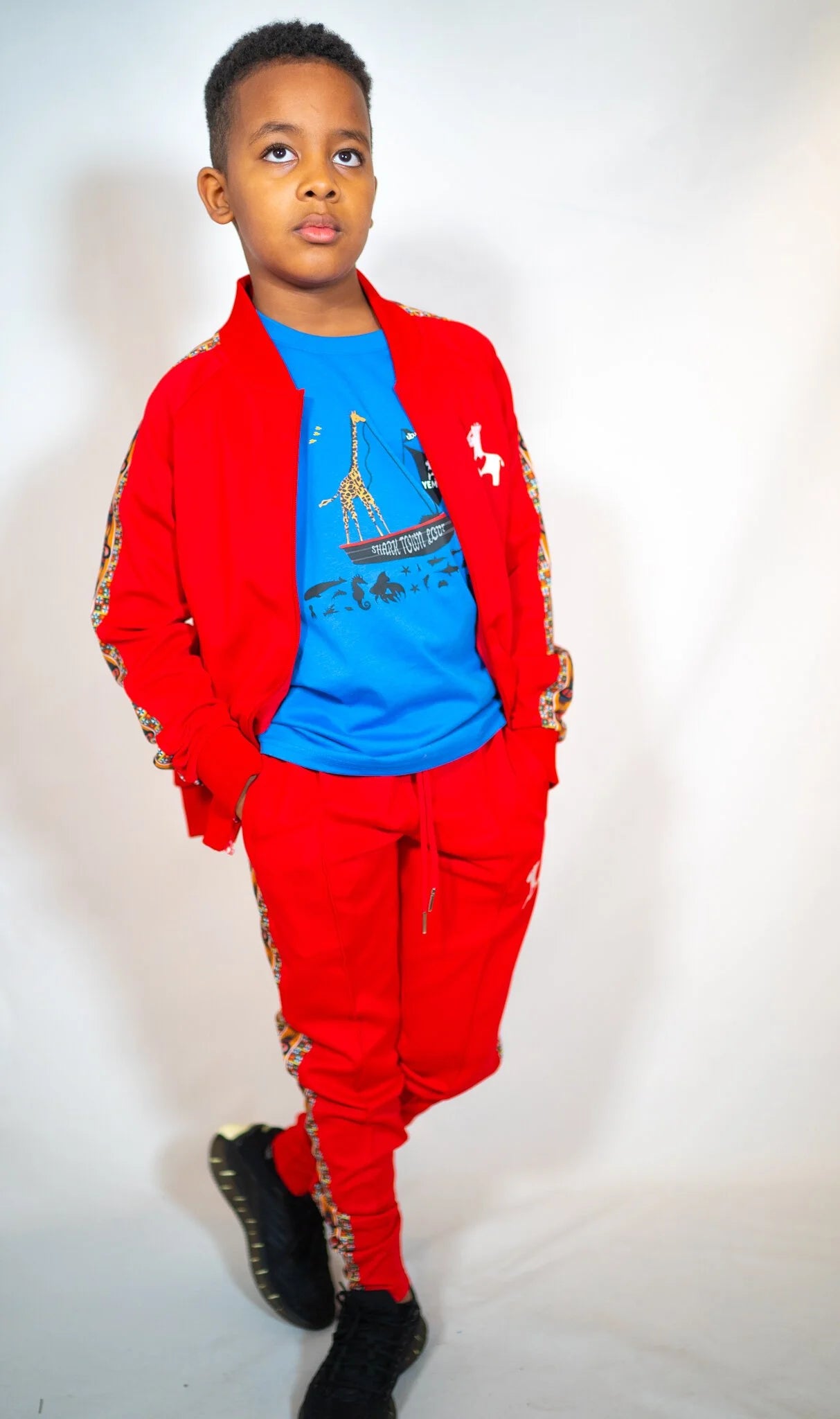Kids' track pants with YEMA giraffe logo and Lali Red colorway honoring Lalibela, Ethiopia
