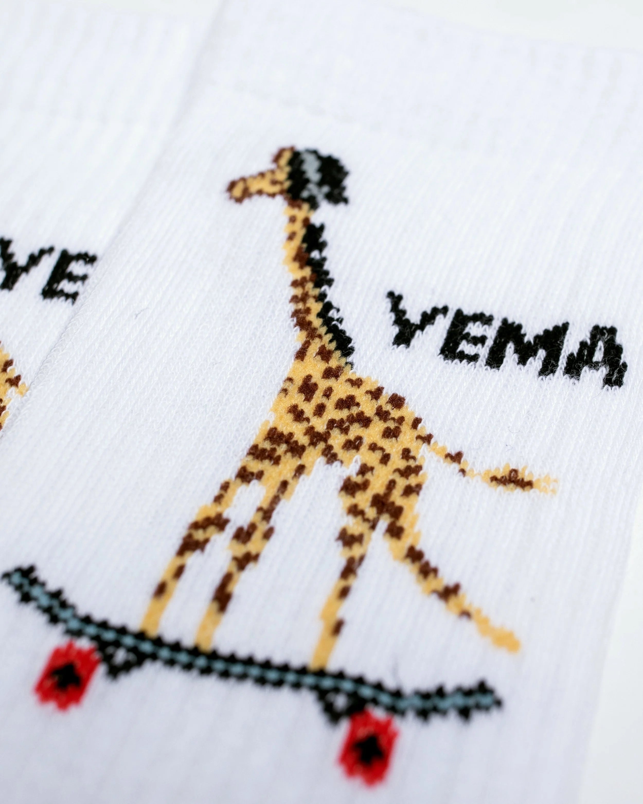 Close-up of YEMA white cotton socks showing skating giraffe motif with orange and black accents
